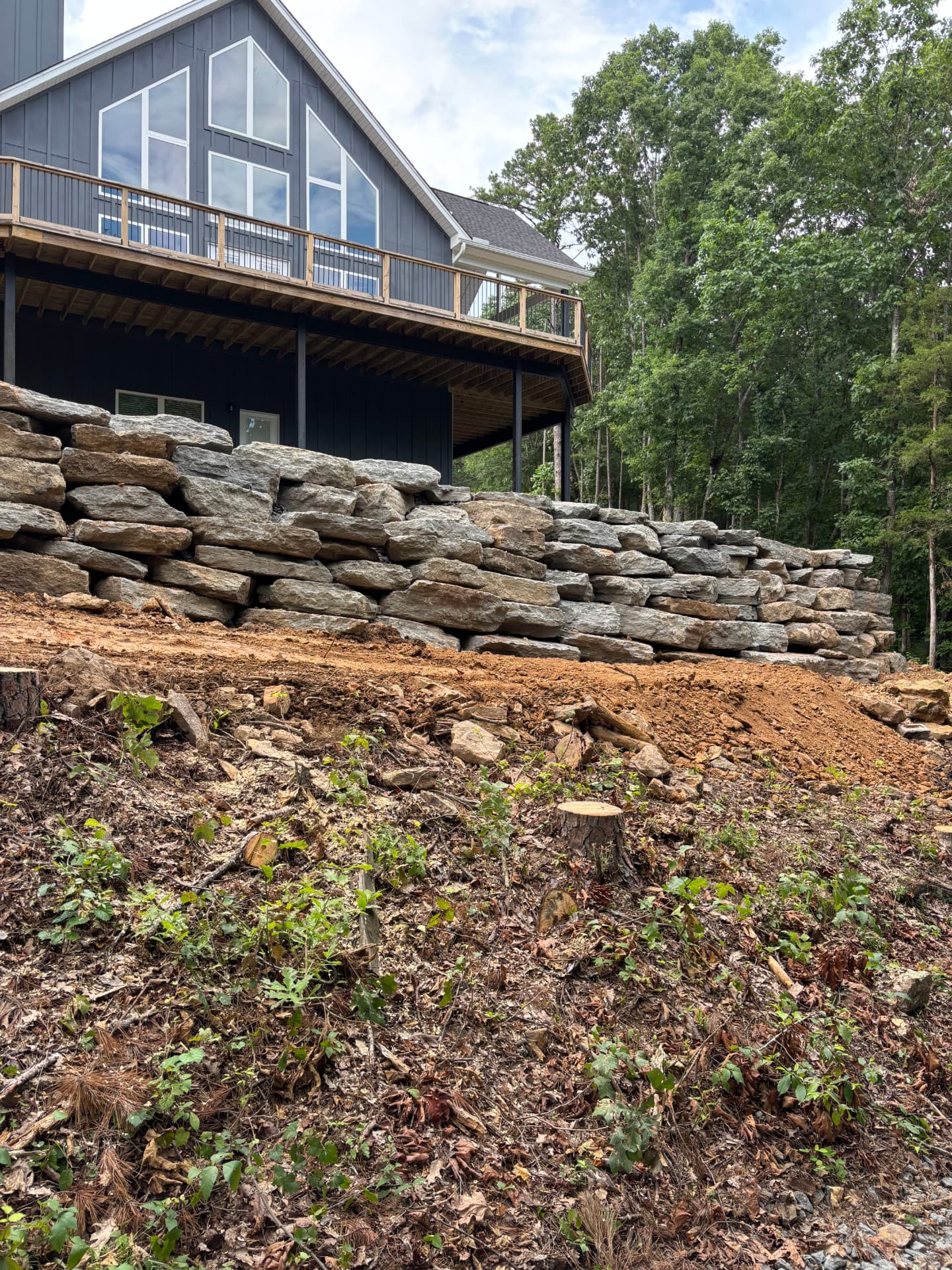 Stacked stone wall holding a steep lot below a new lake house.