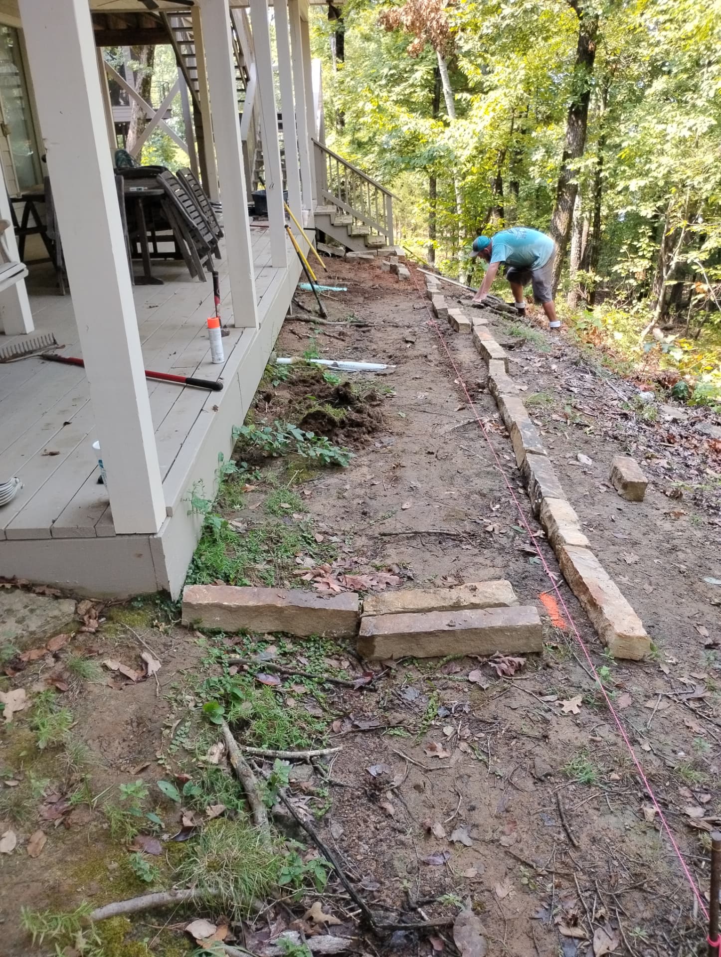 Worker placing stone edging along a dirt path next to a wooden deck before gravel bed installation in Greers Ferry, Arkansas