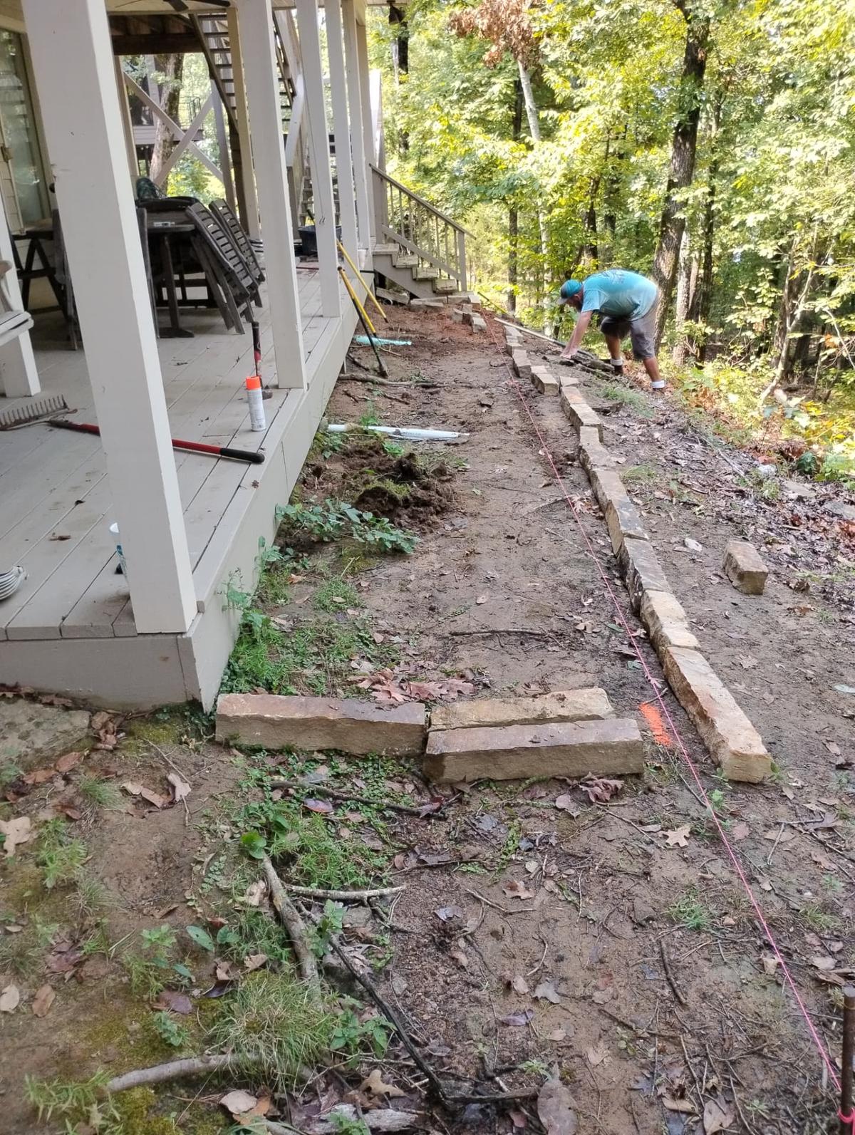 Worker placing stone edging along a dirt path next to a wooden deck before gravel bed installation in Greers Ferry, Arkansas
