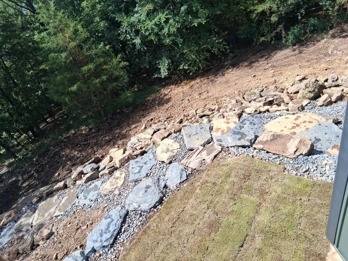 Graded hillside with stepping stones, rock-lined drainage and new sod after landscaping in Heber Springs, Arkansas