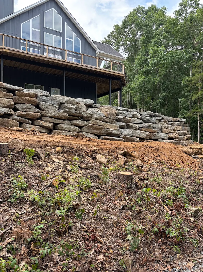 Stacked boulder retaining wall and cleared lot below a new lake house in Greers Ferry, Arkansas