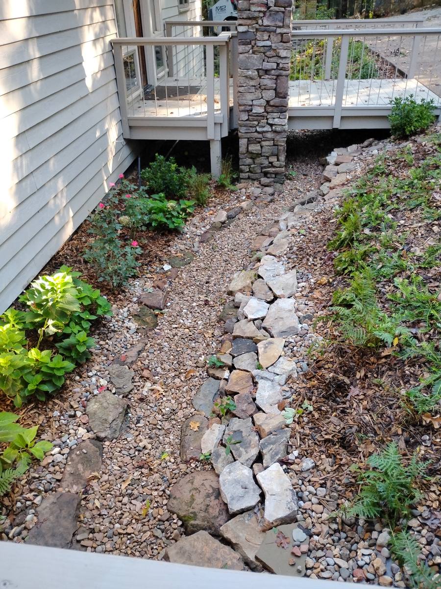 Rock channel routing water past a deck footing and away from the house.