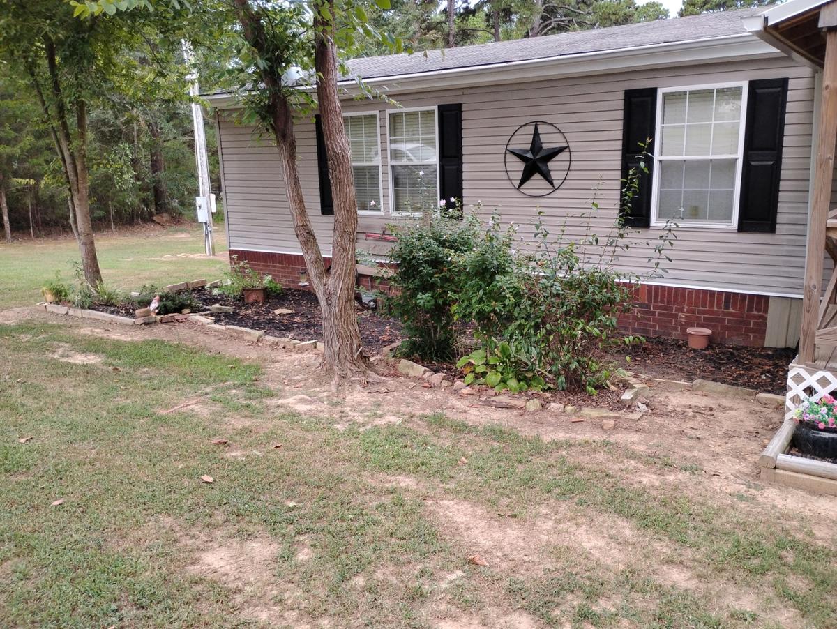 Overgrown mulch flower bed with scattered stone edging beside a house in Greers Ferry, Arkansas