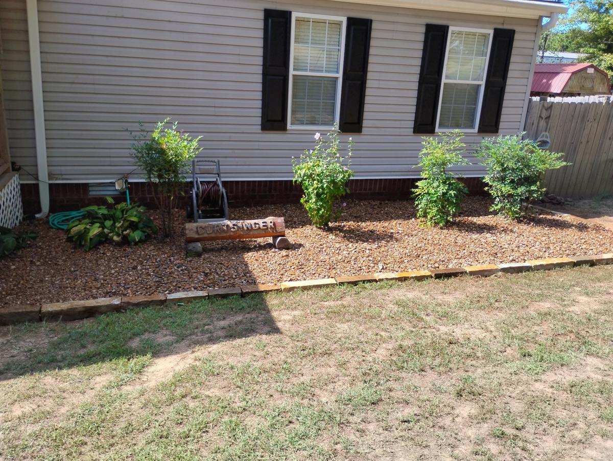 Gravel landscape bed with shrubs and natural stone edging beside a house in Greers Ferry, Arkansas